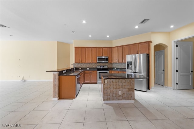 2628 Fairmont Cove Ct, Cape Coral, FL 33991 - kitchen featuring appliances with stainless steel finishes, tasteful backsplash, a peninsula, light tile patterned floors, and arched walkways