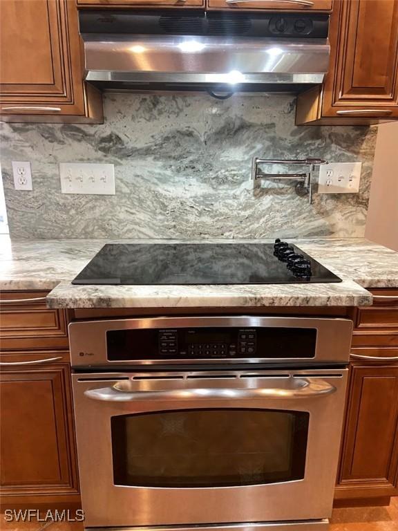 914 Avery St E, Lehigh Acres, FL 33974 - kitchen with under cabinet range hood, stainless steel oven, brown cabinets, and backsplash