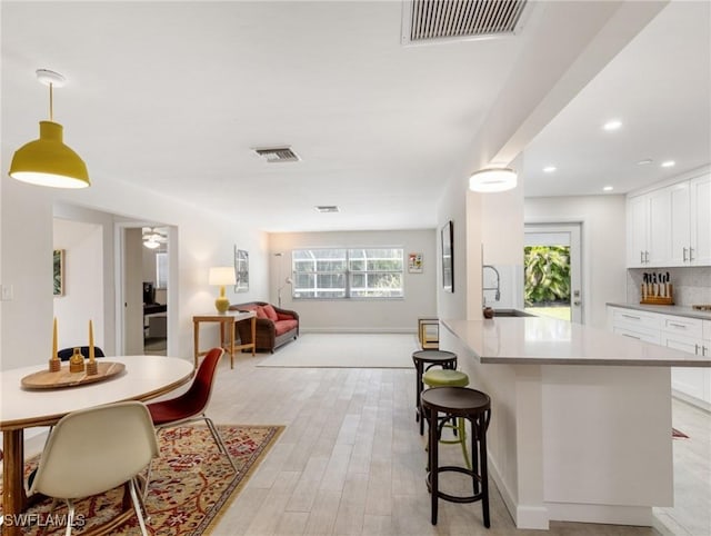 3704 Blue Heron Dr, Fort Myers, FL 33908 - kitchen featuring open floor plan, white cabinets, light wood-style flooring, a kitchen breakfast bar, and backsplash