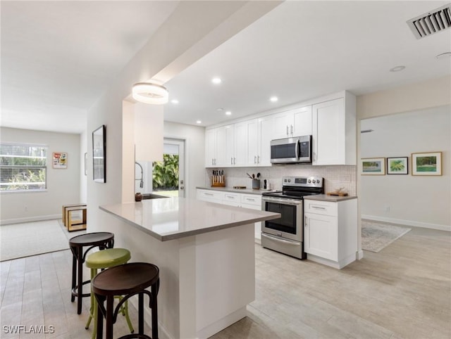 3704 Blue Heron Dr, Fort Myers, FL 33908 - kitchen featuring stainless steel appliances, a breakfast bar area, light wood-type flooring, white cabinets, and recessed lighting
