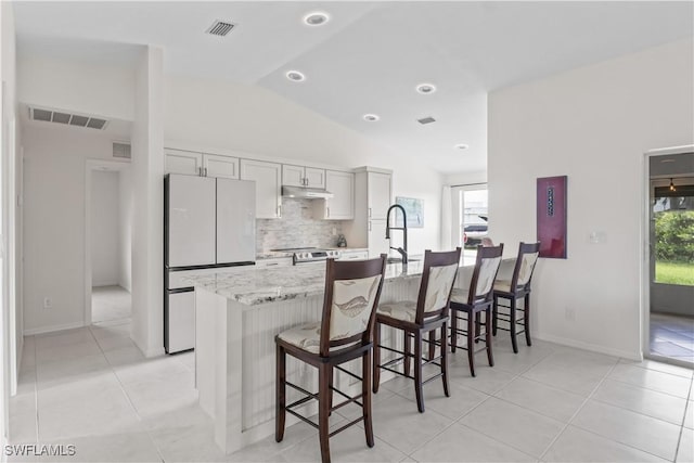 22 NW 14th Ave, Cape Coral, FL 33993 - kitchen with freestanding refrigerator, under cabinet range hood, decorative backsplash, a kitchen breakfast bar, and vaulted ceiling