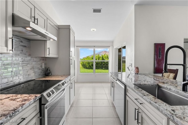 22 NW 14th Ave, Cape Coral, FL 33993 - kitchen with appliances with stainless steel finishes, under cabinet range hood, decorative backsplash, light tile patterned floors, and light stone countertops