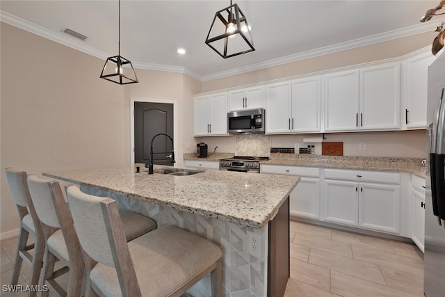 17573 Ashcomb Way, Estero, FL 33928 - kitchen with stainless steel appliances, white cabinets, a center island with sink, light stone countertops, and crown molding