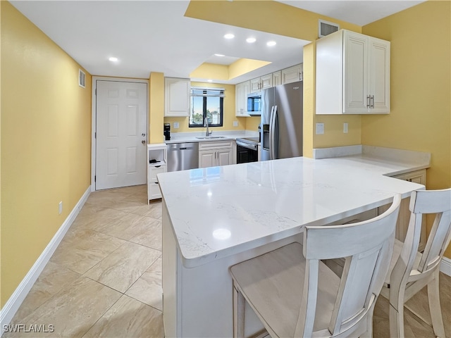 4770 Estero Blvd Unit 203, Fort Myers Beach, FL 33931 - kitchen with appliances with stainless steel finishes, a peninsula, a breakfast bar, light stone counters, and white cabinets