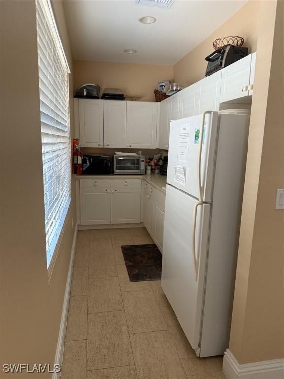 1520 SW 50th St Unit 101, Cape Coral, FL 33914 - kitchen featuring freestanding refrigerator, plenty of natural light, white cabinets, and light tile patterned floors