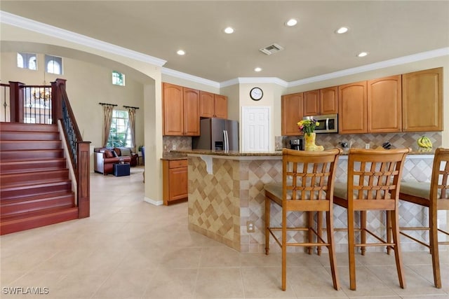 5730 Lago Villaggio Way, Naples, FL 34104 - kitchen with stainless steel appliances, a kitchen bar, backsplash, dark stone countertops, and ornamental molding
