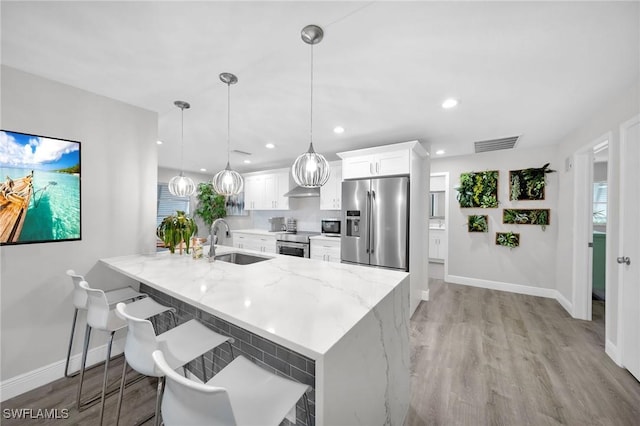 1138 Lucerne Ave, Cape Coral, FL 33904 - kitchen with appliances with stainless steel finishes, white cabinets, light wood finished floors, light stone countertops, and a breakfast bar area