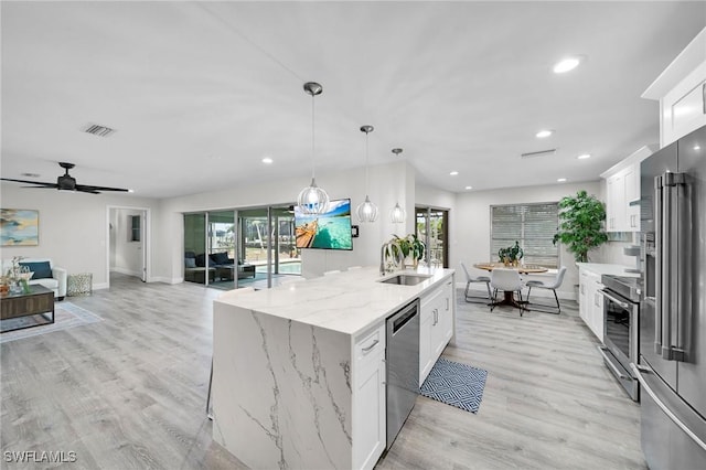 1138 Lucerne Ave, Cape Coral, FL 33904 - kitchen featuring appliances with stainless steel finishes, white cabinets, an island with sink, open floor plan, and light wood-style flooring