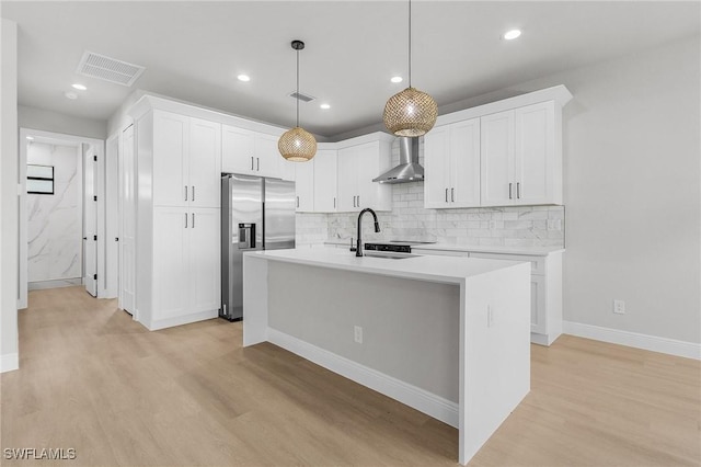 1299 Argosy Rd, Labelle, FL 33935 - kitchen featuring stainless steel fridge, light wood-style flooring, decorative backsplash, wall chimney exhaust hood, and a center island with sink