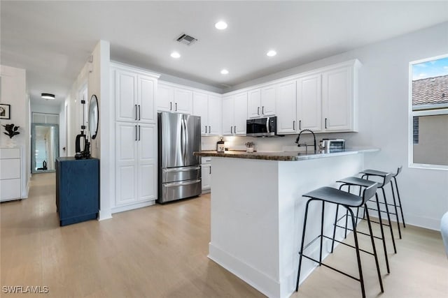 10490 Spruce Pine Ct, Fort Myers, FL 33913 - kitchen featuring appliances with stainless steel finishes, a peninsula, a kitchen bar, dark countertops, and white cabinets