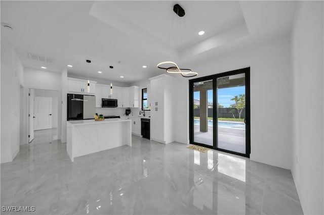2018 Nelson Rd N, Cape Coral, FL 33993 - kitchen featuring refrigerator, black microwave, white cabinetry, a kitchen island, and decorative light fixtures