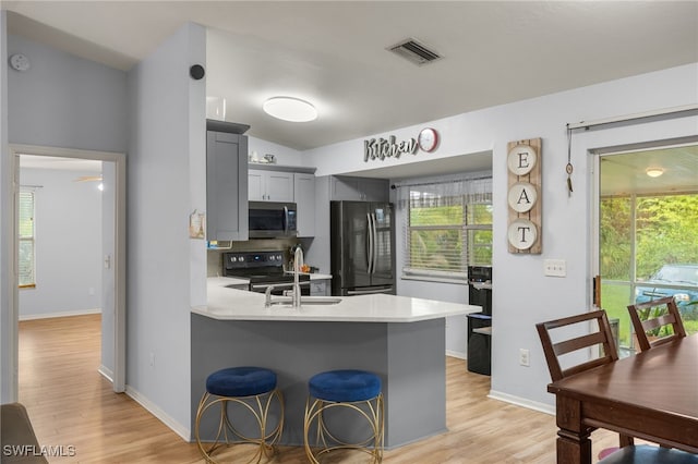 343 Golden Gate Blvd E, Naples, FL 34120 - kitchen featuring black appliances, light countertops, a peninsula, light wood-type flooring, and a kitchen breakfast bar