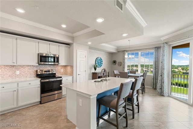10720 Palazzo Way Unit 405, Fort Myers, FL 33913 - kitchen featuring appliances with stainless steel finishes, ornamental molding, decorative backsplash, light tile patterned flooring, and a center island with sink