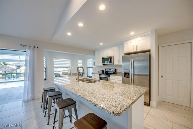 2812 SW 46th Ter, Cape Coral, FL 33914 - kitchen with appliances with stainless steel finishes, a kitchen island with sink, white cabinets, a breakfast bar, and light tile patterned floors