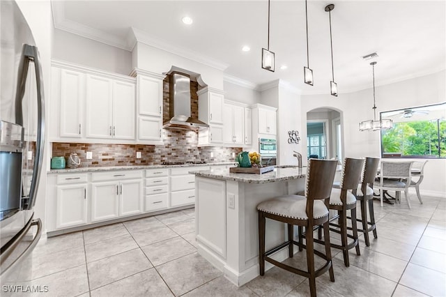 1387 Mockingbird Dr, Naples, FL 34120 - kitchen with stainless steel appliances, wall chimney exhaust hood, tasteful backsplash, white cabinets, and ornamental molding