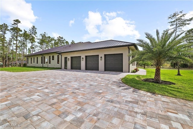 5174 Sycamore Dr, Naples, FL 34119 - view of front facade featuring stucco siding, decorative driveway, a garage, a front lawn, and a standing seam roof