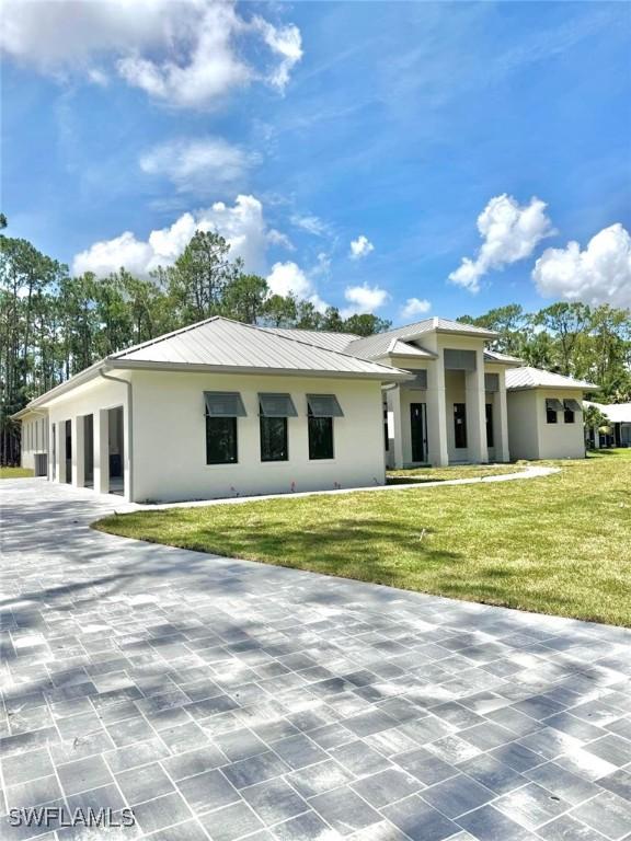 5174 Sycamore Dr, Naples, FL 34119 - view of front of property with stucco siding, a front lawn, a metal roof, and a standing seam roof