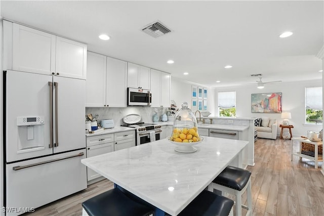719 Park Ave, Naples, FL 34110 - kitchen with stainless steel appliances, a peninsula, white cabinetry, light wood-type flooring, and open floor plan