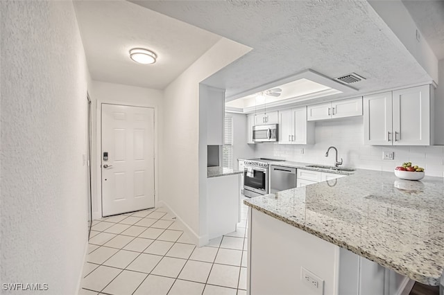 16251 Dublin Cir Unit F101, Fort Myers, FL 33908 - kitchen with appliances with stainless steel finishes, light tile patterned floors, white cabinetry, light stone counters, and a peninsula