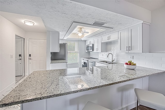16251 Dublin Cir Unit F101, Fort Myers, FL 33908 - kitchen with stainless steel microwave, light stone countertops, a peninsula, a textured ceiling, and a breakfast bar