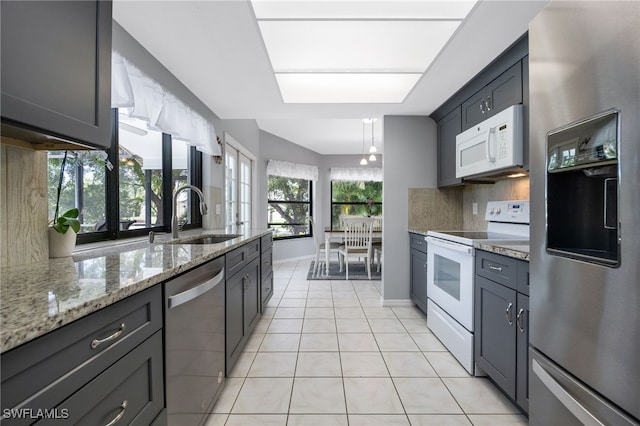 kitchen with appliances with stainless steel finishes, backsplash, light tile patterned floors, light stone countertops, and gray cabinets