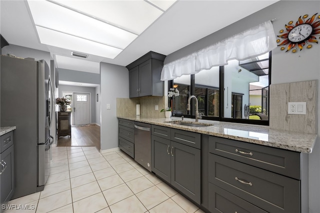 kitchen featuring appliances with stainless steel finishes, light tile patterned floors, gray cabinetry, and light stone counters