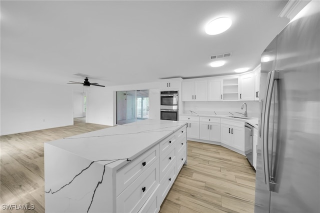 3307 Pinetree St, Port Charlotte, FL 33952 - kitchen with appliances with stainless steel finishes, a kitchen island, white cabinets, light stone counters, and light wood-style flooring