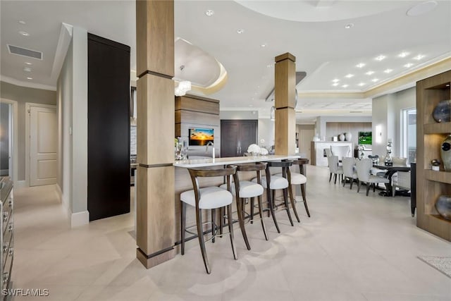 kitchen with ornamental molding, modern cabinets, a kitchen bar, recessed lighting, and a tray ceiling