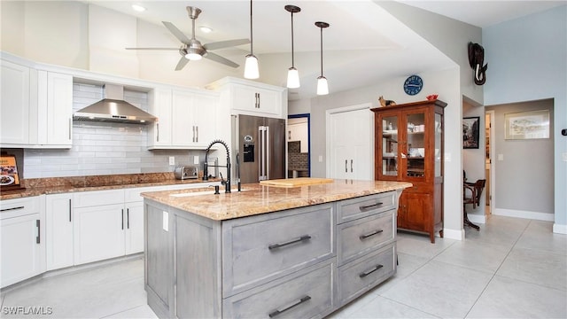5961 Sea Grass Ln, Naples, FL 34116 - kitchen with high end refrigerator, decorative backsplash, a ceiling fan, wall chimney exhaust hood, and light stone counters