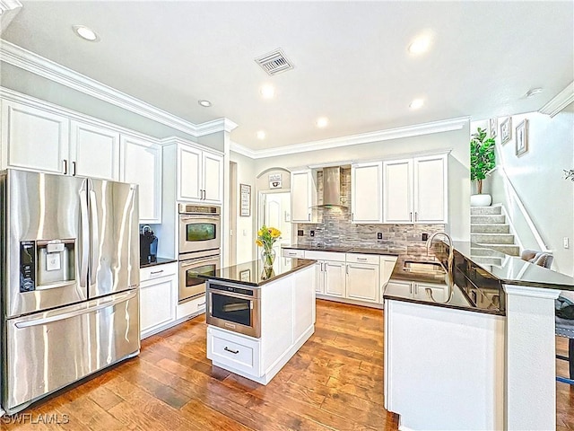 3032 Via Rialto St, Fort Myers, FL 33905 - kitchen with stainless steel appliances, dark countertops, wall chimney range hood, hardwood / wood-style floors, and white cabinets