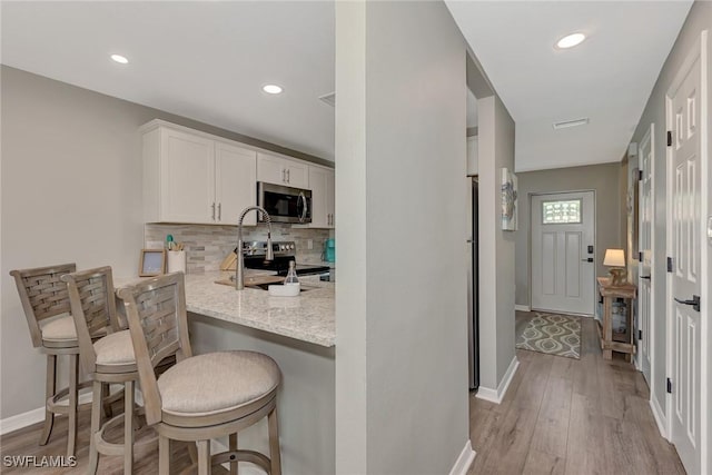 1752 Stickney Point Rd Unit 102, Sarasota, FL 34231 - kitchen with stainless steel appliances, decorative backsplash, white cabinetry, a kitchen breakfast bar, and light wood-style flooring