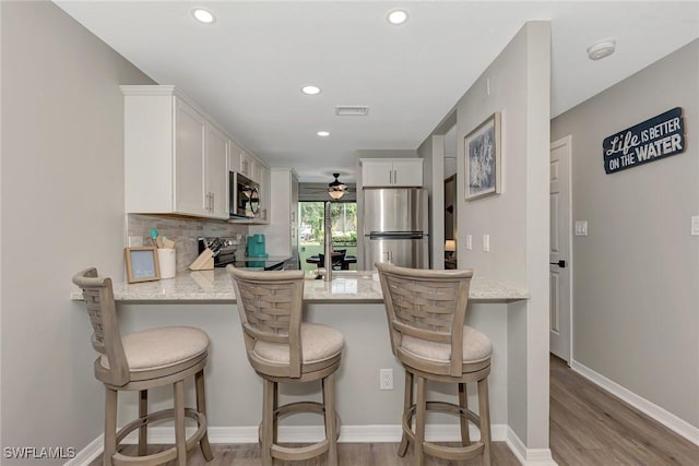 1752 Stickney Point Rd Unit 102, Sarasota, FL 34231 - kitchen featuring appliances with stainless steel finishes, light wood-style flooring, a peninsula, white cabinets, and backsplash