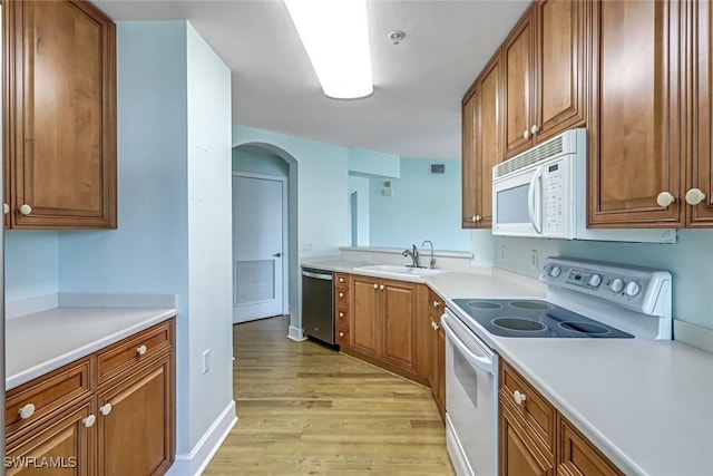 3082 Windsong Ct Unit 303, Naples, FL 34109 - kitchen featuring white appliances, light wood finished floors, arched walkways, brown cabinetry, and light countertops