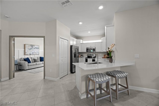 9051 Leatherwood Loop, Lehigh Acres, FL 33936 - kitchen with stainless steel appliances, a peninsula, a kitchen breakfast bar, white cabinetry, and light countertops