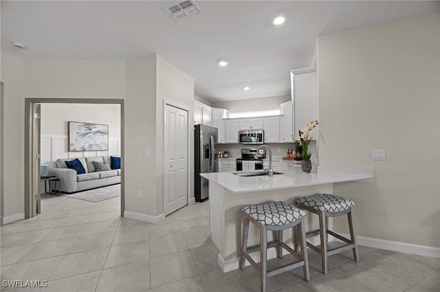 9051 Leatherwood Loop, Lehigh Acres, FL 33936 - kitchen featuring appliances with stainless steel finishes, a peninsula, a breakfast bar area, white cabinetry, and light countertops