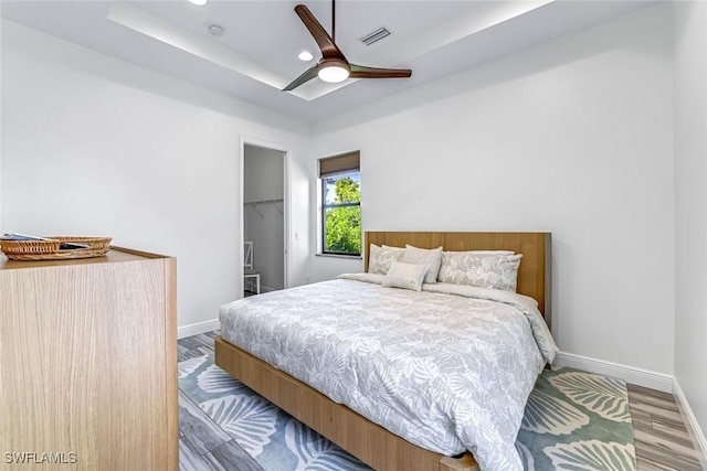 3980 Full Moon Ct, Naples, FL 34112 - bedroom with wood finished floors, a tray ceiling, recessed lighting, ceiling fan, and a walk in closet