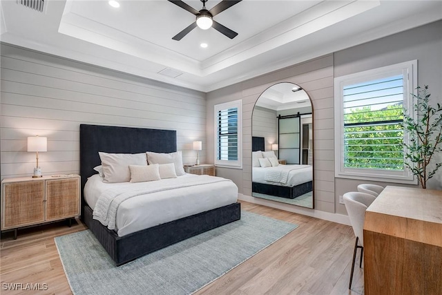 234 Legacy Ct, Naples, FL 34110 - bedroom with a raised ceiling, a barn door, wood walls, light wood-style flooring, and recessed lighting