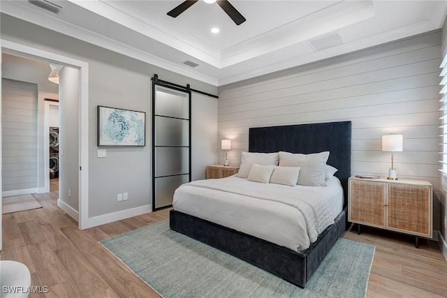 234 Legacy Ct, Naples, FL 34110 - bedroom with a barn door, wood walls, light wood-style flooring, a tray ceiling, and recessed lighting