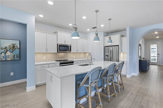 19387 Elston Way, Estero, FL 33928 - kitchen with stainless steel appliances, arched walkways, backsplash, a center island with sink, and white cabinets