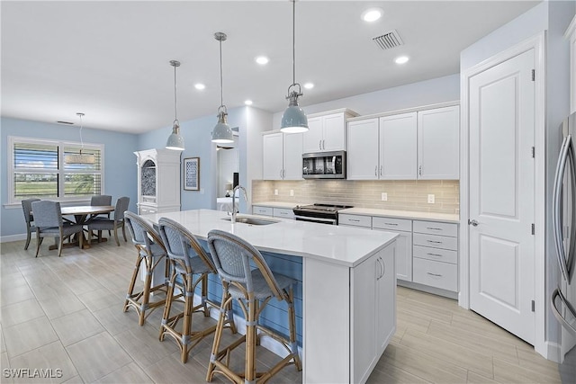 19387 Elston Way, Estero, FL 33928 - kitchen featuring appliances with stainless steel finishes, tasteful backsplash, light countertops, an island with sink, and a kitchen bar