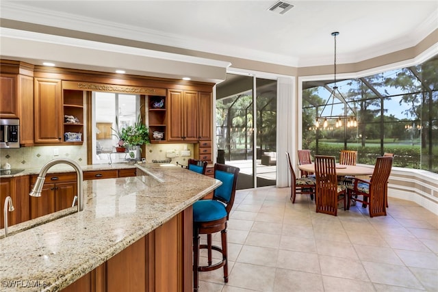 4323 Silver Fox Dr, Naples, FL 34119 - kitchen with open shelves, brown cabinets, stainless steel microwave, light stone countertops, and ornamental molding