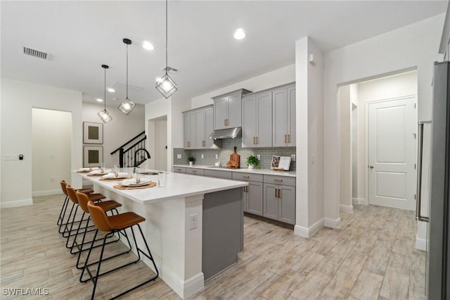 3240 Pilot Cir, Naples, FL 34120 - kitchen featuring gray cabinets, light countertops, light wood-type flooring, a breakfast bar, and backsplash