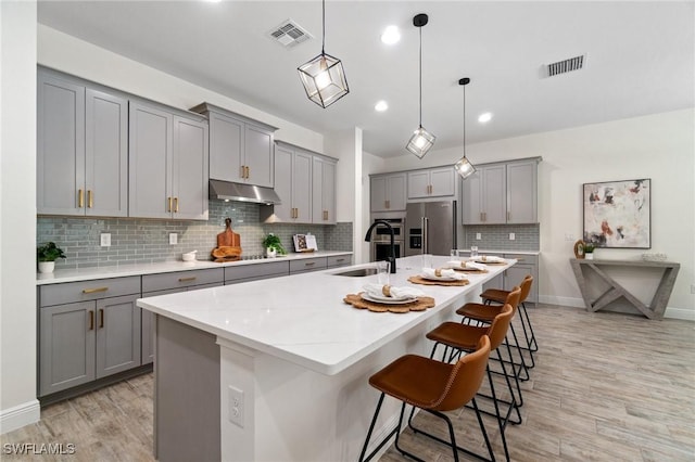 3240 Pilot Cir, Naples, FL 34120 - kitchen featuring gray cabinets, high quality fridge, under cabinet range hood, light wood-style flooring, and decorative backsplash