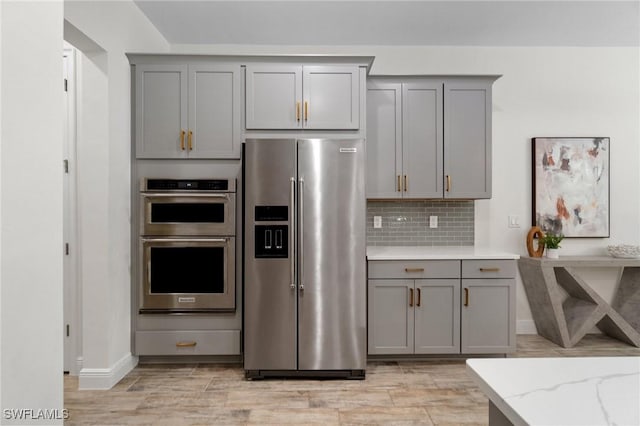3240 Pilot Cir, Naples, FL 34120 - kitchen with stainless steel appliances, gray cabinetry, backsplash, and light wood finished floors