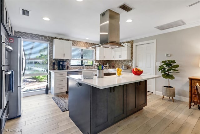 1015 El Valle Ave, Fort Myers, FL 33919 - kitchen with island range hood, white cabinetry, light countertops, light wood-style flooring, and ornamental molding