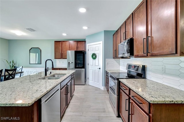 692 Hadley St E, Naples, FL 34104 - kitchen with stainless steel appliances, light wood-type flooring, light stone countertops, backsplash, and a kitchen island with sink
