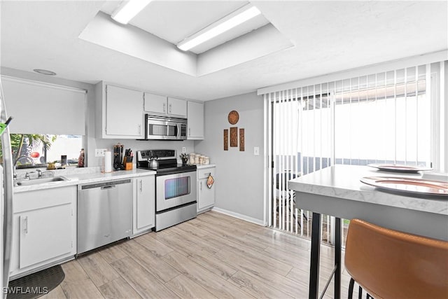 9761 Maplecrest Cir, Lehigh Acres, FL 33936 - kitchen with stainless steel appliances, light countertops, a raised ceiling, white cabinetry, and light wood-style floors