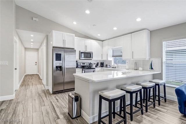 851 102nd Ave N, Naples, FL 34108 - kitchen featuring appliances with stainless steel finishes, a peninsula, white cabinets, a kitchen breakfast bar, and lofted ceiling