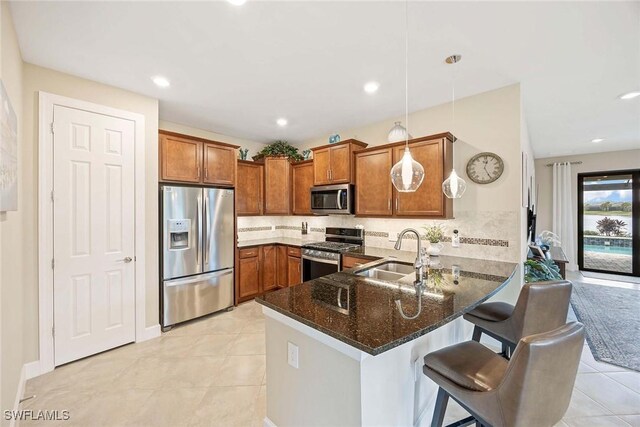 7773 Jacaranda Ln, Naples, FL 34114 - kitchen with stainless steel appliances, a peninsula, brown cabinetry, dark stone countertops, and tasteful backsplash