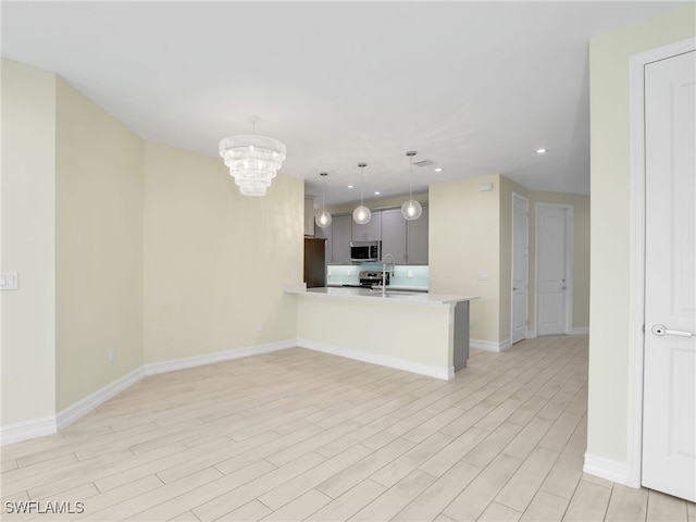 7524 Carnegie Way, Naples, FL 34119 - kitchen with appliances with stainless steel finishes, a chandelier, light countertops, a peninsula, and light wood-style flooring